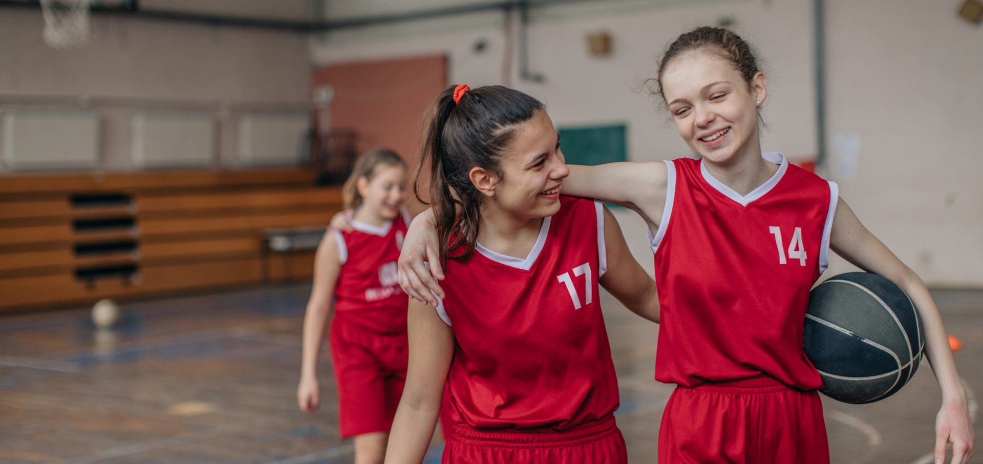 Girls in red basketball jerseys smiling and walking together.