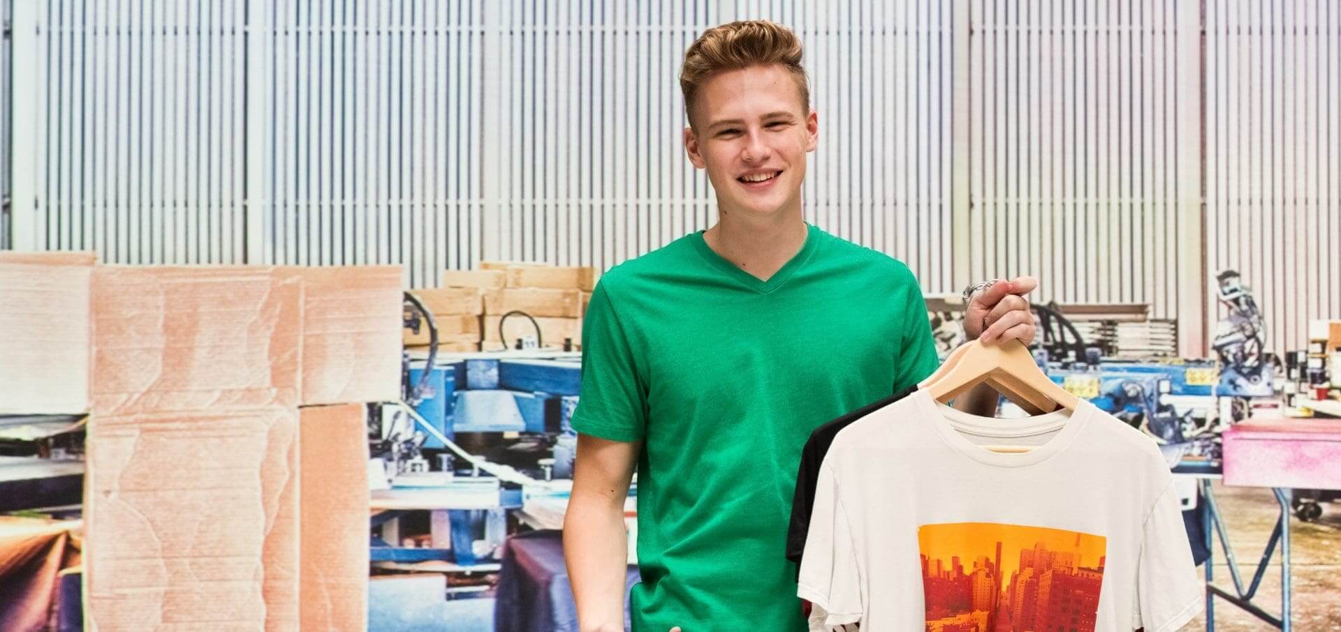 Smiling young man in a green shirt near a clothing rack.
